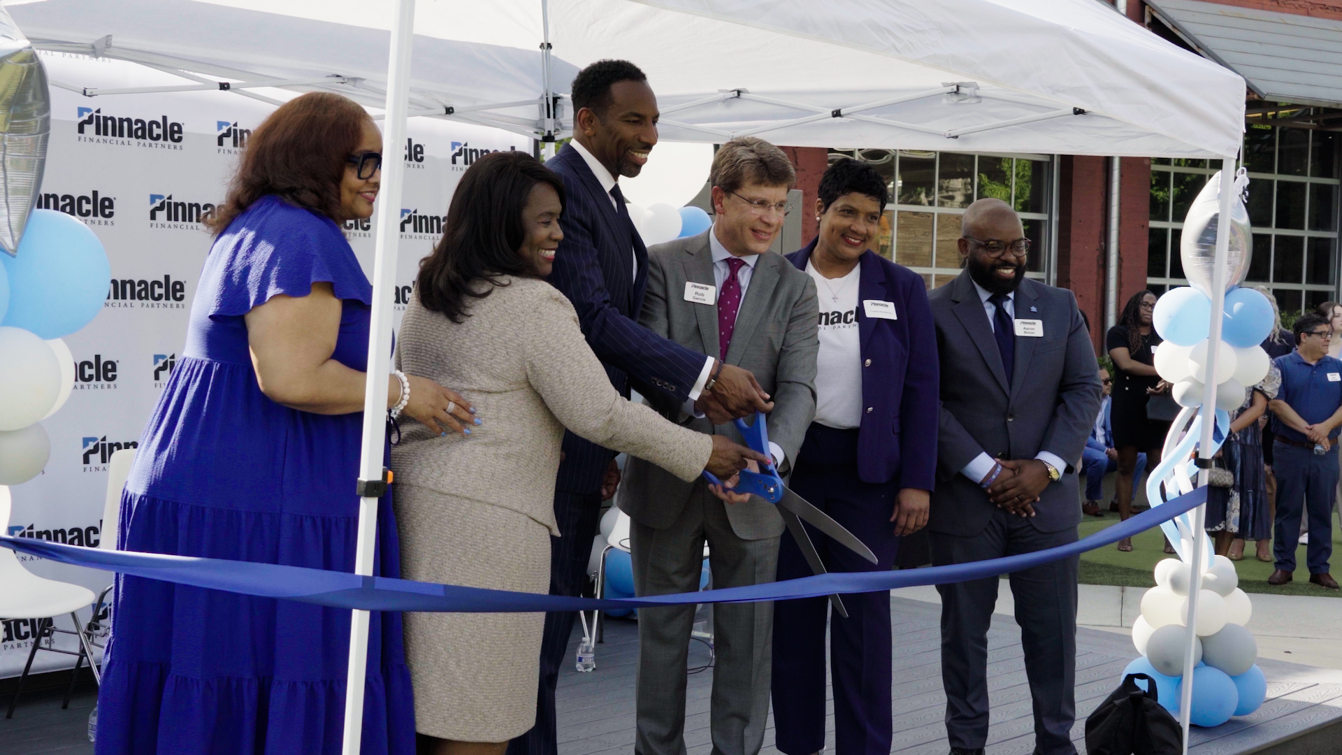 People gathered to cut a blue ribbon.